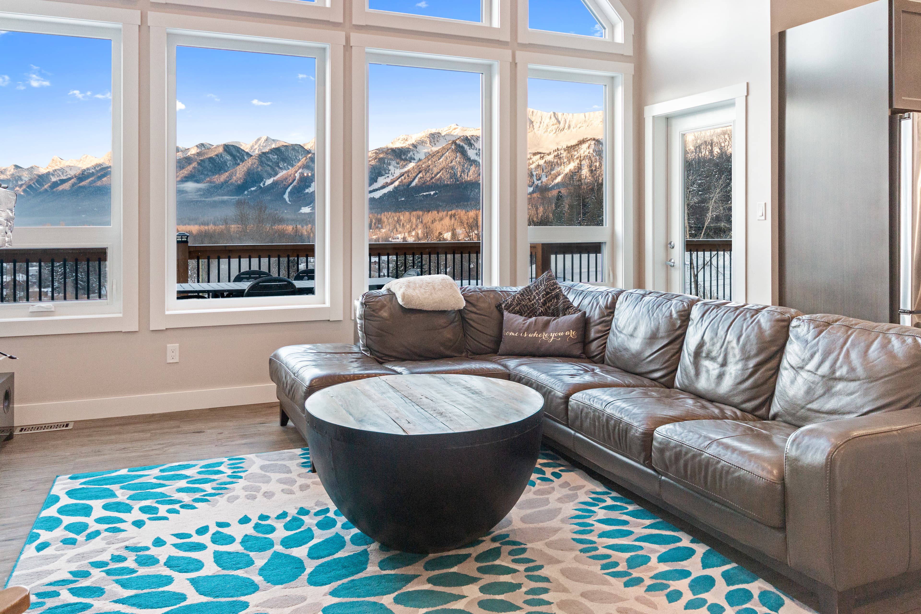 Living room of The Perch, its floor-to-ceiling windows framing the snow-covered ski runs of Fernie Alpine Resort across the valley